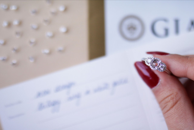 Platinring mit drei funkelnden Diamanten in Halo-Fassung, gehalten zwischen roten Fingernägeln. Ihr Schmuck bei BAUNAT maßangefertigt.