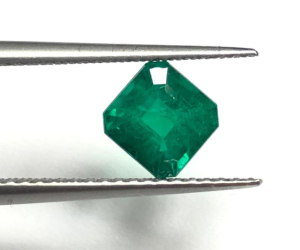 Grüner, facettierter Smaragd im Diamantschliff zwischen Metallpinzetten
