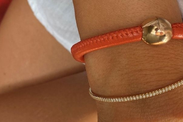 Orangefarbenes Lederarmband mit Goldkugel und feines Goldarmband mit kleinen Diamanten am Handgelenk
