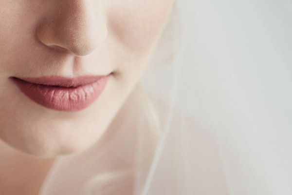 Nahaufnahme einer Braut mit zartem Schleier und rosigen Lippen, romantisches Hochzeitsmotiv