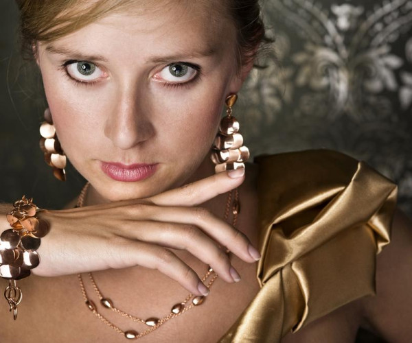 Frau mit breiten Rotgold-Ohrringen und Armband sowie filigraner Rotgoldkette mit glänzenden runden Elementen