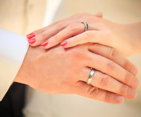 Nahaufnahme von zwei Händen mit schlichten Eheringen aus Weißgold, ein Ring mit kleinem Diamantbesatz.