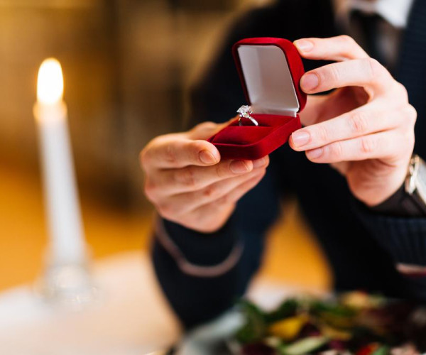 Mann hält roten Samt-Ringkasten mit Solitär-Diamant-Verlobungsring aus Weißgold