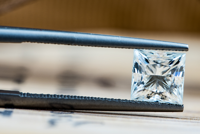 Quadratischer Princess-Diamant im Brillantschliff, gehalten von einer dunklen Pinzette Prinzessinnen-Diamantschliff - BAUNAT