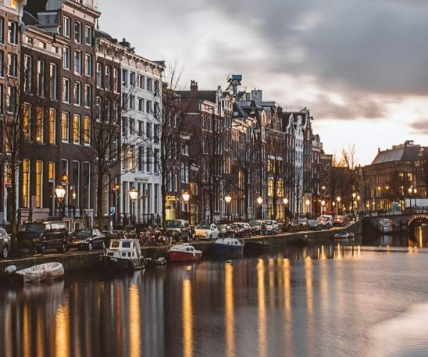 Amsterdamer Grachtenkanal bei Sonnenuntergang mit historischen Häusern und Brücke