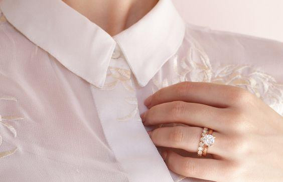 Hand mit goldfarbenem Verlobungsring mit großem Diamanten und Pavé-Besatz an weißem Hemd