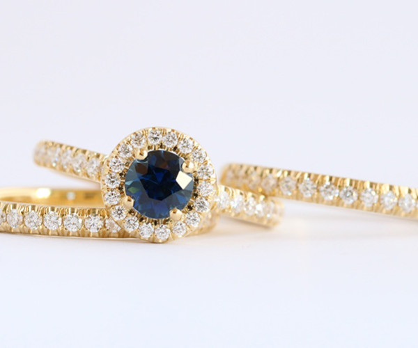 Gelbgoldener Verlobungsring mit blauem Mittelstein und Halo-Fassung aus kleinen Diamanten