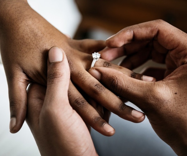 Hände beim Anstecken eines Solitär-Diamantrings aus Weißgold mit pavébesetzter Ringschiene