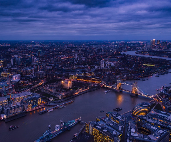 Luftaufnahme von London bei Abenddämmerung mit Tower Bridge, Themse und beleuchteter Skyline.