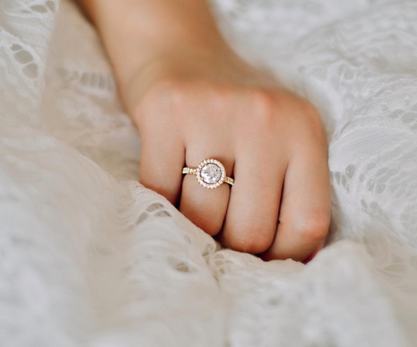 Hand mit Roségold-Verlobungsring, runder Diamant im Halo-Fassung und pavébesetztem Band
