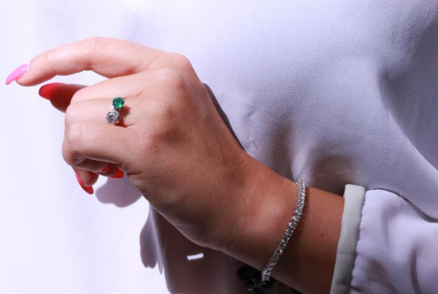 Hand mit grünem Smaragd-Ring und Diamant-Cocktailring sowie Tennisarmband aus Weißgold