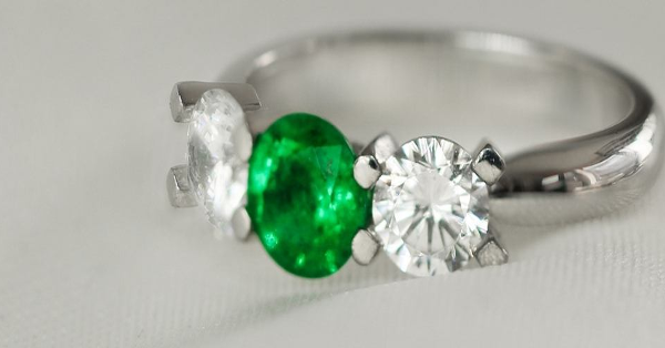 Ein Ring mit drei Smaragden, die von funkelnden Diamanten umgeben sind und Eleganz und Luxus in seinem Design zeigen.