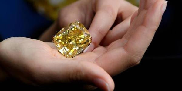 Großer gelber Diamant im Kissenschliff, in Händen präsentiert, mit facettiertem Glanz und goldener Fassung