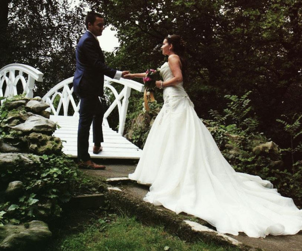 Brautpaar auf weißer Brücke: Braut im schulterfreien Satin-Brautkleid mit Schleier und Blumenstrauß