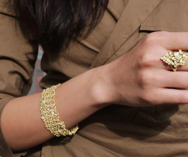 Eine Frau, die ein goldenes Kettenarmband und einen goldenen Ring an ihrer Hand trägt und eleganten Schmuck hervorhebt.
