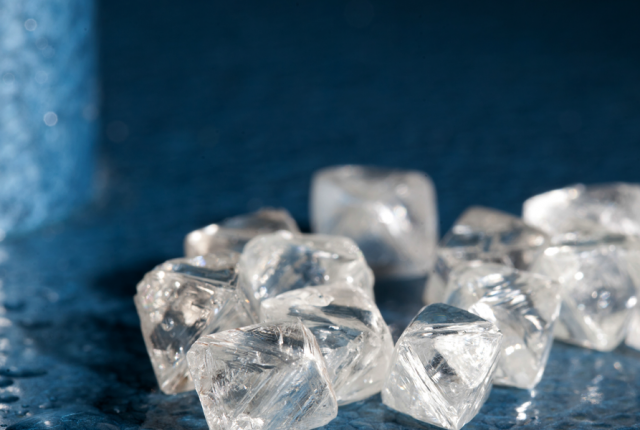 Close-up of rough, uncut diamonds on a dark blue surface with cool lighting