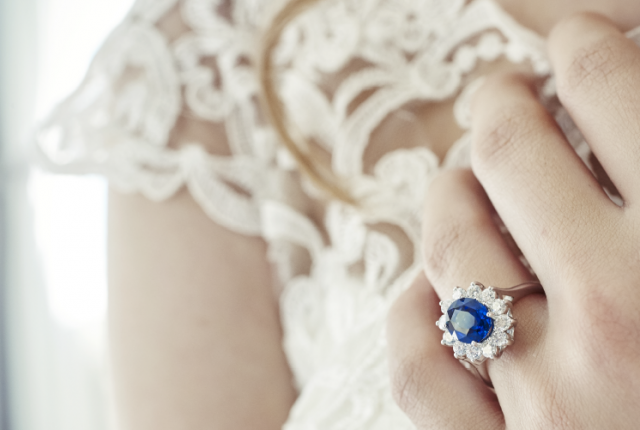 A close-up of a woman’s left hand wearing a wedding ring, prominently featuring a blue sapphire gemstone