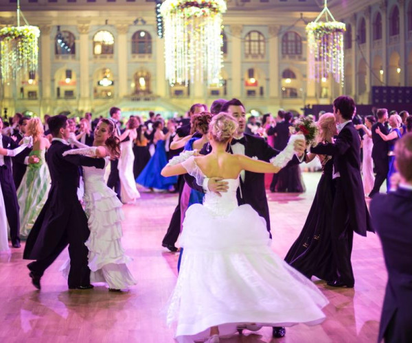 Elegant couples ballroom dancing in formal evening gowns and black tuxedos under grand chandeliers