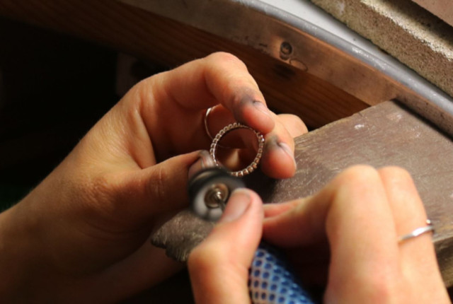 Jeweler polishing a rose gold diamond ring on a workbench, showing a pavé setting in progress.
