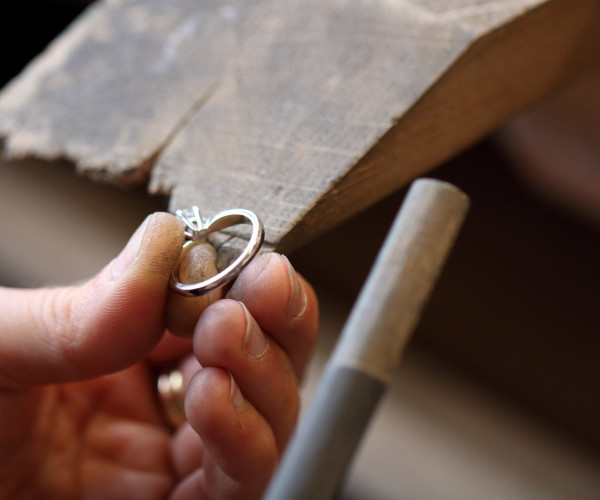 Jeweler holding a white gold engagement ring with a prong-set diamond under a workbench