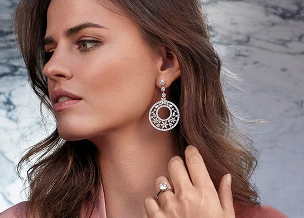 A woman showcasing large diamond earrings, highlighting their brilliance and elegance against her attire
