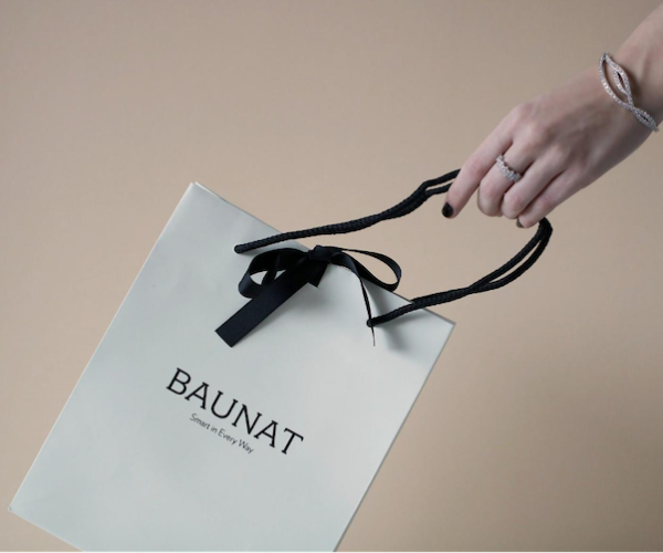A person holding a white shopping bag from BAUNAT after buying jewellery