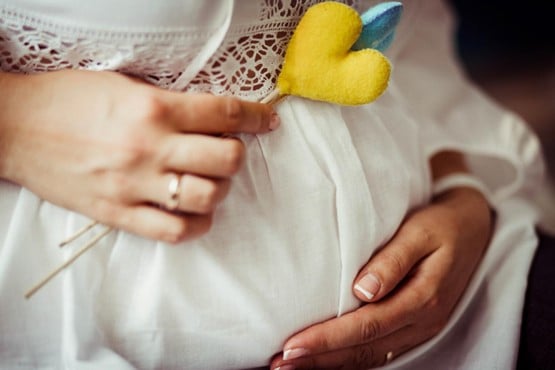 : Pregnant woman holding her belly, her hands displaying a ring
