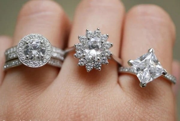 A close-up of a woman's hand adorned with multiple diamond engagement rings, each featuring a distinct and unique design.