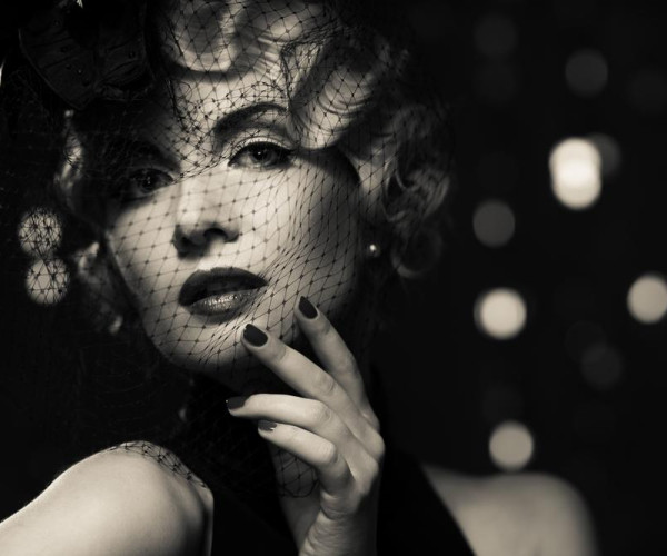 Black-and-white portrait of a woman in a black veil, wearing a pearl stud earring and dark lipstick