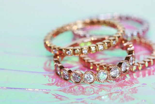 Anillos de oro rosa con diamantes talla brillante engastados en halo, apilados sobre fondo pastel Descubre las colecciones de BAUNAT