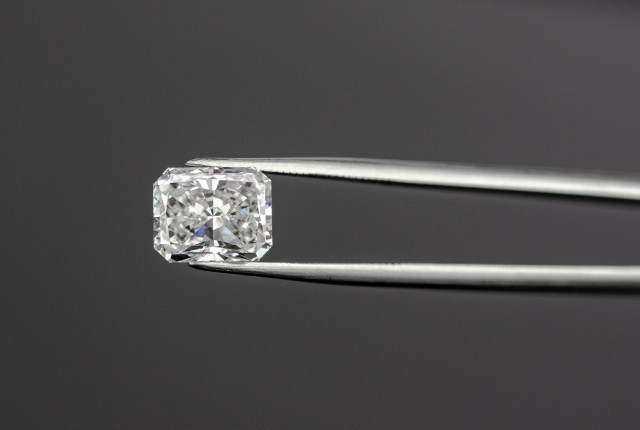 Diamante radiante tallado, sujeto con pinzas metálicas sobre fondo oscuro El diamante en talla radiant es el anillo de compromiso perfecto - BAUNAT
