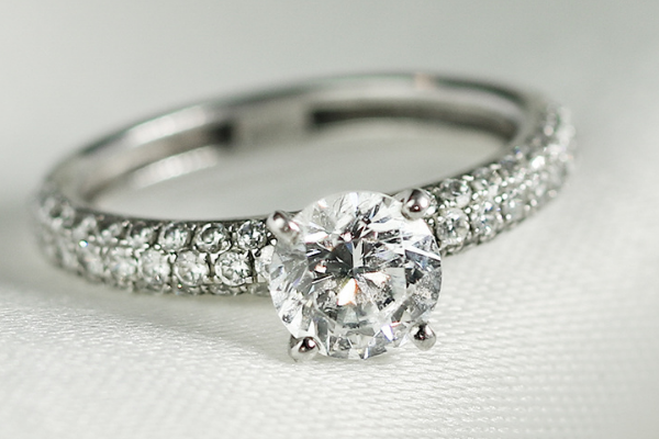 Anillo de compromiso de oro blanco con diamante central en talla brillante y pavé de diamantes