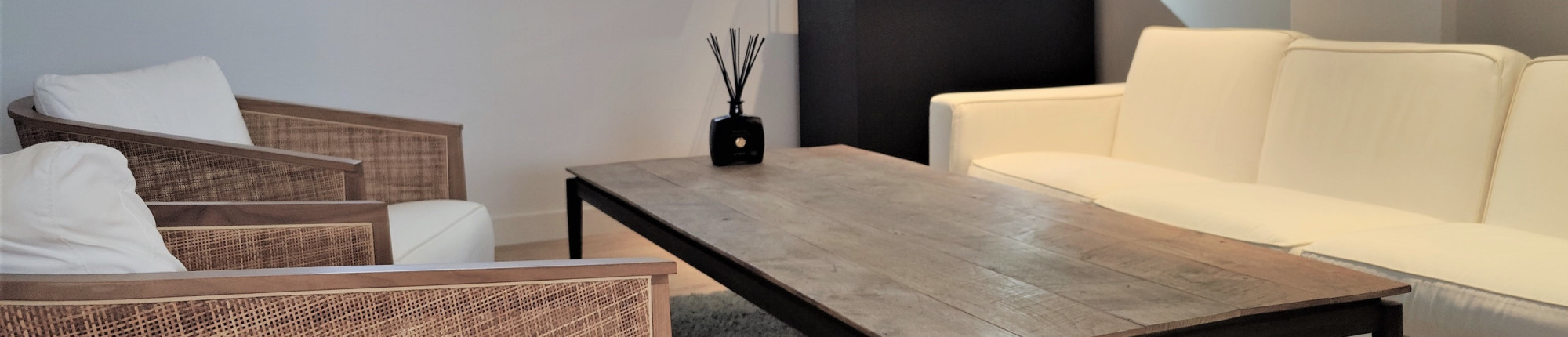 Showroom con cita de BAUNAT con sillones de mimbre, sofá blanco y mesa de madera