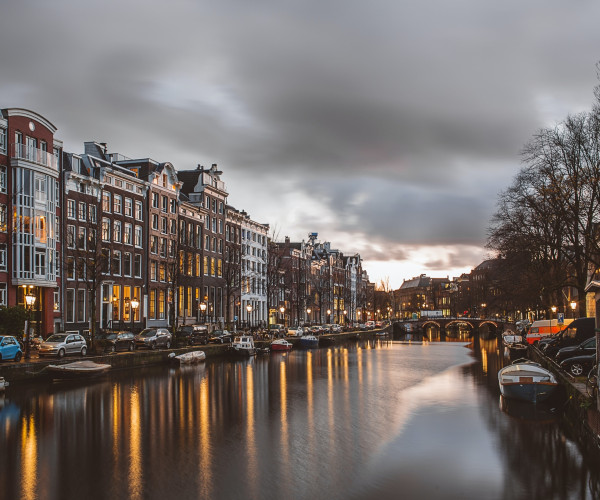 Canal de Ámsterdam al atardecer, con casas históricas, puentes y reflejos dorados en el agua