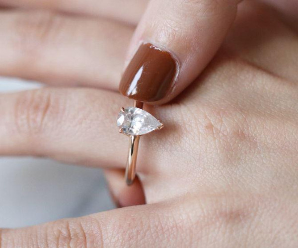 Anillo de oro rosa con diamante talla pera montado en bisel, sobre una mano