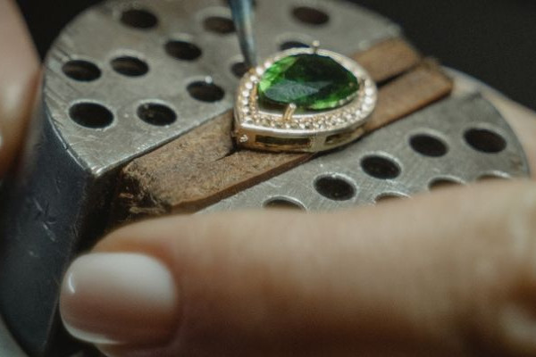 Anillo de oro amarillo con gema verde en corte pera y halo de pequeños diamantes, sujeto en banco de joyero