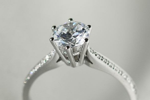 Anillo de compromiso en oro blanco con diamante redondo en engaste de cuatro garras y pavé lateral