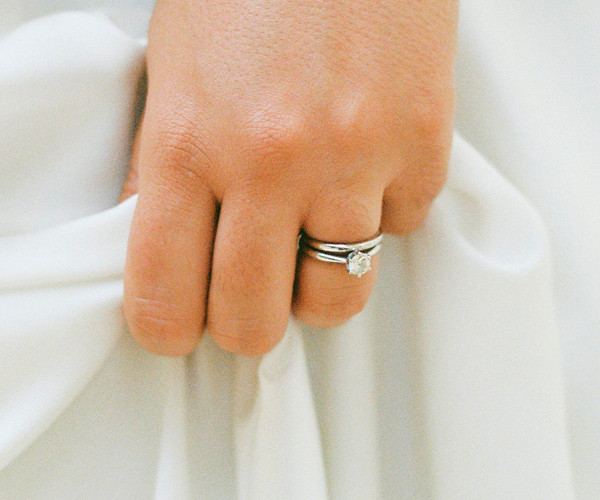 Mano con anillo de compromiso de oro blanco y diamante talla brillante sobre vestido blanco