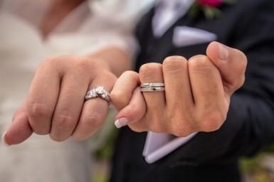 Manos de pareja con anillos de boda en oro blanco: alianza lisa y sortija con diamante central