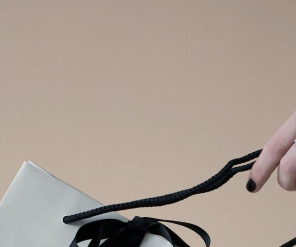 main de femme portant un bracelet manchette avec motif ondulé tenant un sac blanc avec un ruban noir