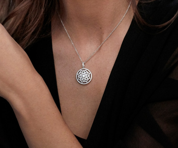 Collier pendentif rond en or blanc serti de diamants, motif floral délicat, porté avec une bague diamant assortie.