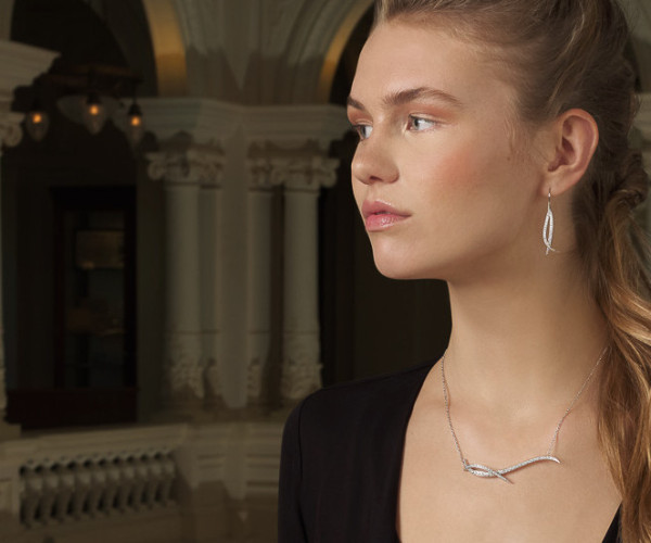 Collier en or blanc avec pendentif courbe pavé de diamants, porté avec boucles d’oreilles assorties.
