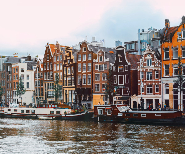 Canal d’Amsterdam bordé de maisons historiques à pignons, avec bateaux amarrés au premier plan.