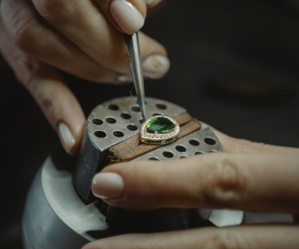 des mains habiles travaillant sur une bague ornée d'une pierre émeraude verte, mettant en valeur le savoir-faire en matière de sertissage de diamants