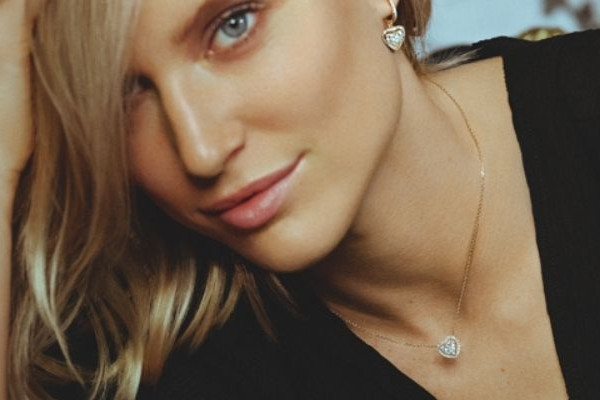 Femme portant un collier fin en or blanc avec pendentif cœur serti de diamants et boucles d’oreilles assorties