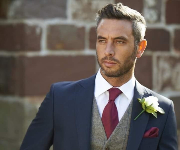 Homme en costume bleu marine portant une petite boucle d’oreille en diamant, style discret et élégant.