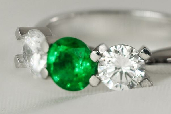 Une bague ornée de trois émeraudes entourées de diamants étincelants, mettant en valeur l'élégance et le luxe dans son design.
