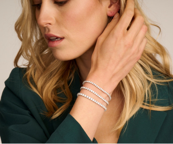 Une femme en chemisier vert présente des bracelets en or superposés à son poignet, mettant en valeur son style élégant