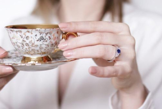 une femme tenant une tasse avec une soucoupe, portant un beau diamant bleu à son doigt