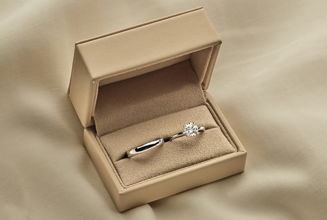 Bague de fiançailles en or blanc avec diamant solitaire, présentée dans un écrin beige.